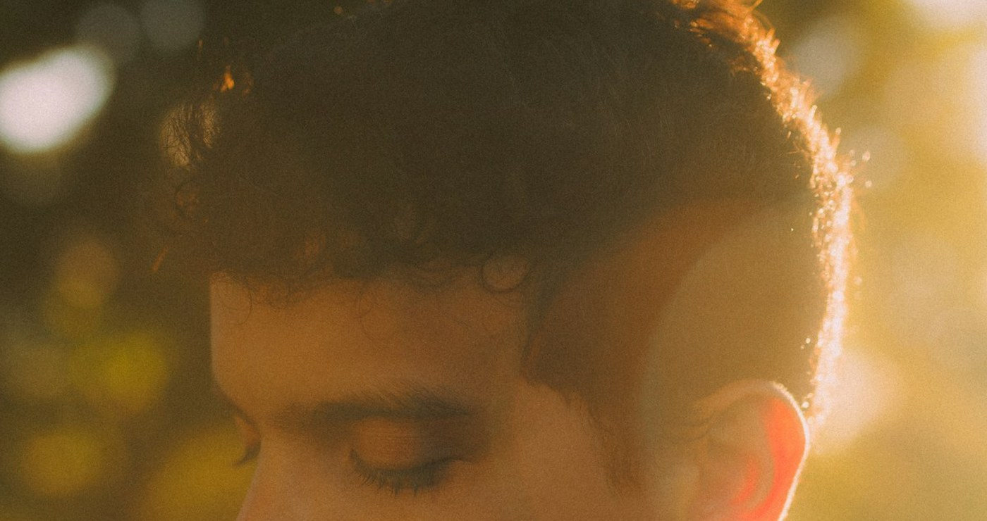 A young man in golden afternoon light, seen close, eyes lowered.