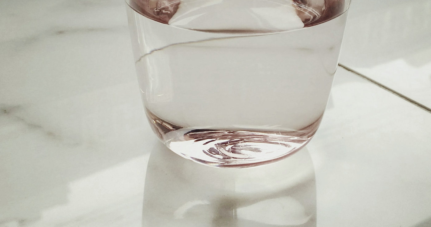 A glass of water on a pale marble surface in bright daylight.
