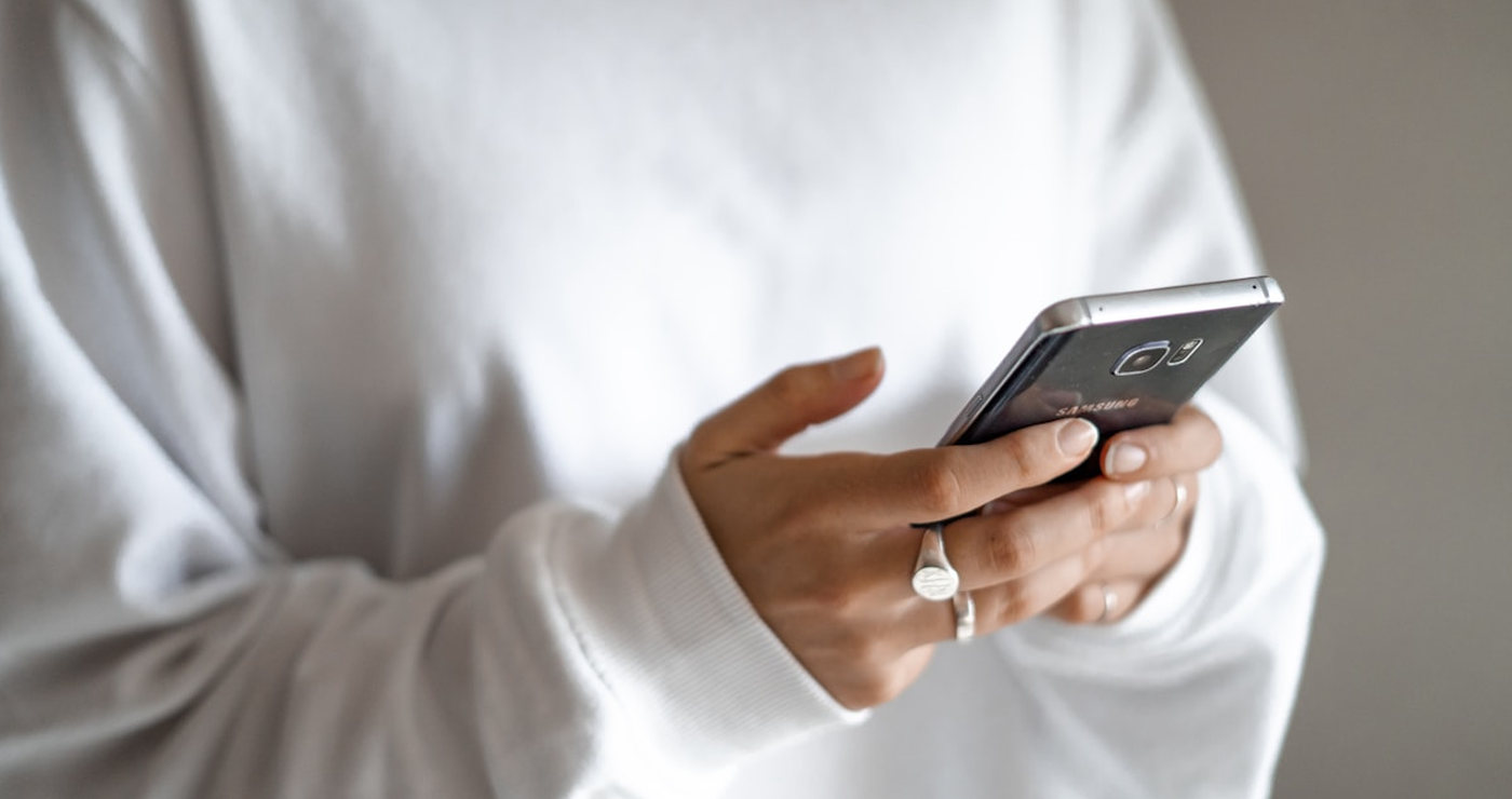 A hand holding a phone, close, against a soft neutral wall.