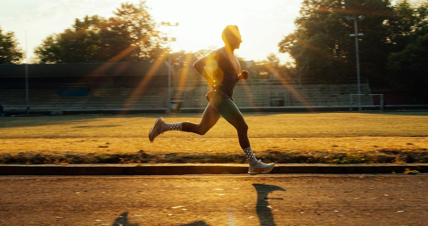 A runner on a track at golden hour, a long shadow thrown across the lane.