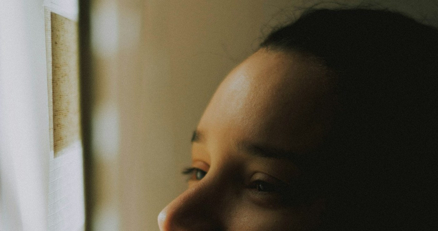 A woman at a window in warm indoor light, seen close, half in shadow.
